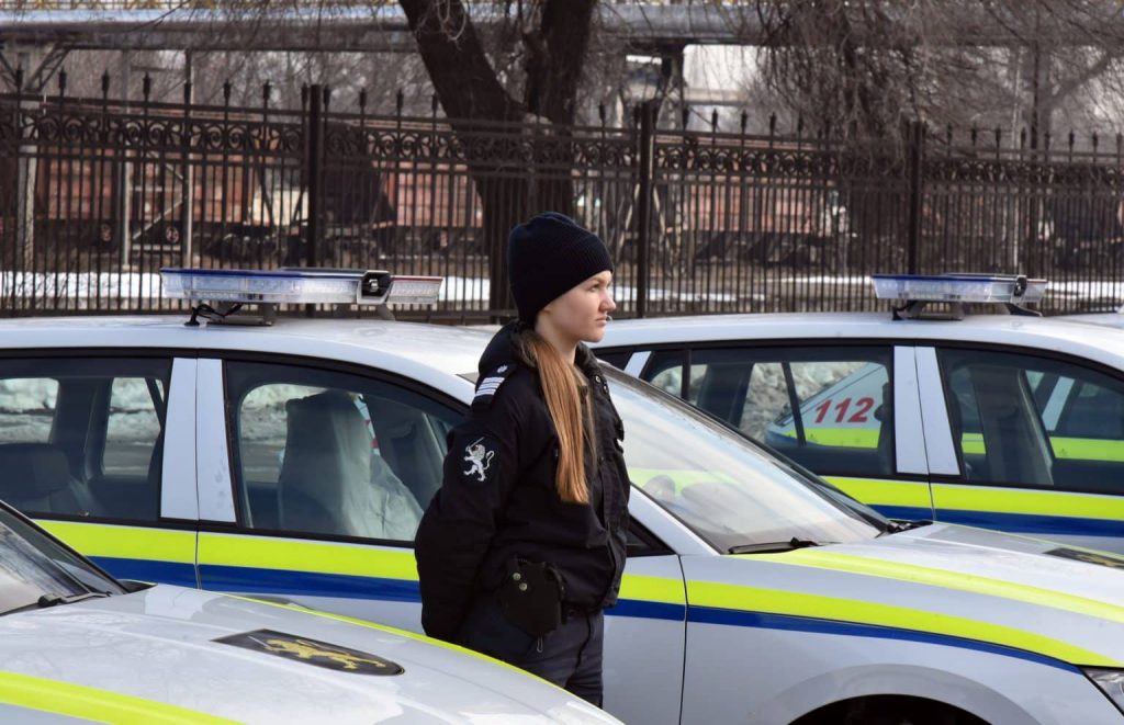 a female police officer looking to the right, standing in between new police cars.