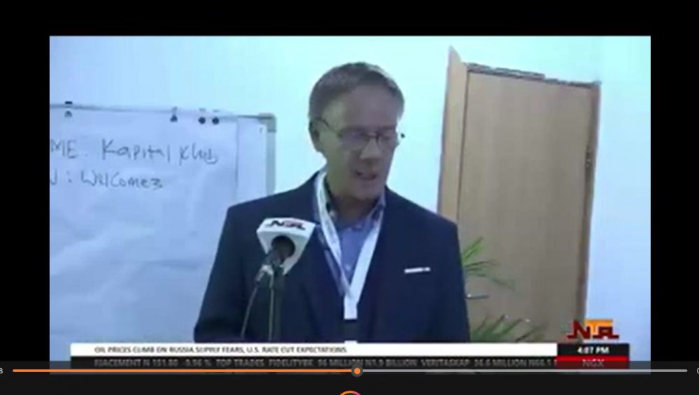 eter Heepen delivers a speech during a Nigerian Television Authority (NTA) news broadcast, standing at a podium with an NTA microphone in front of him and a flip chart in the background.