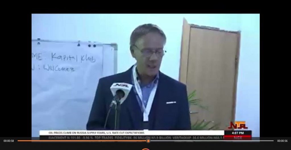 eter Heepen delivers a speech during a Nigerian Television Authority (NTA) news broadcast, standing at a podium with an NTA microphone in front of him and a flip chart in the background.