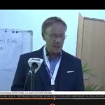 eter Heepen delivers a speech during a Nigerian Television Authority (NTA) news broadcast, standing at a podium with an NTA microphone in front of him and a flip chart in the background.