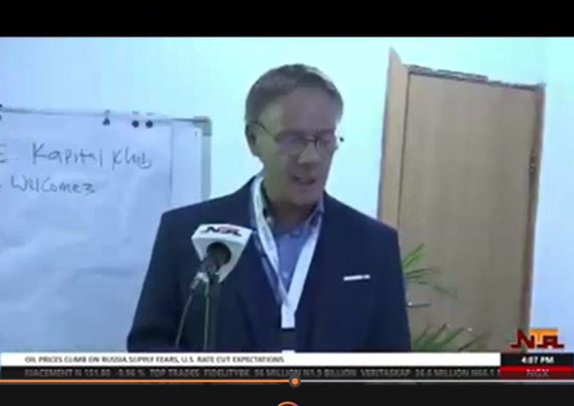 eter Heepen delivers a speech during a Nigerian Television Authority (NTA) news broadcast, standing at a podium with an NTA microphone in front of him and a flip chart in the background.