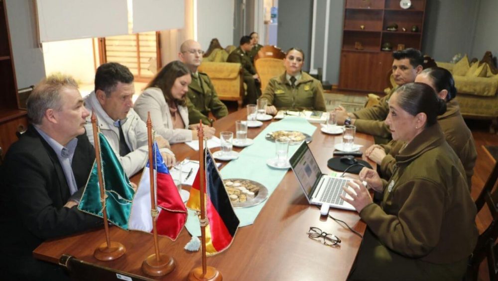 Briefing at Carabineros office; desk flags and laptop in foreground as officers and GS-Foundation delegates confer.