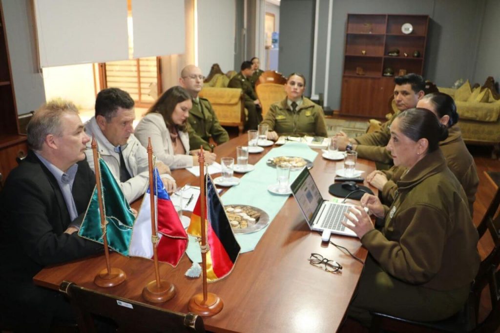 Briefing at Carabineros office; desk flags and laptop in foreground as officers and GS-Foundation delegates confer.