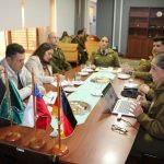 Briefing at Carabineros office; desk flags and laptop in foreground as officers and GS-Foundation delegates confer.