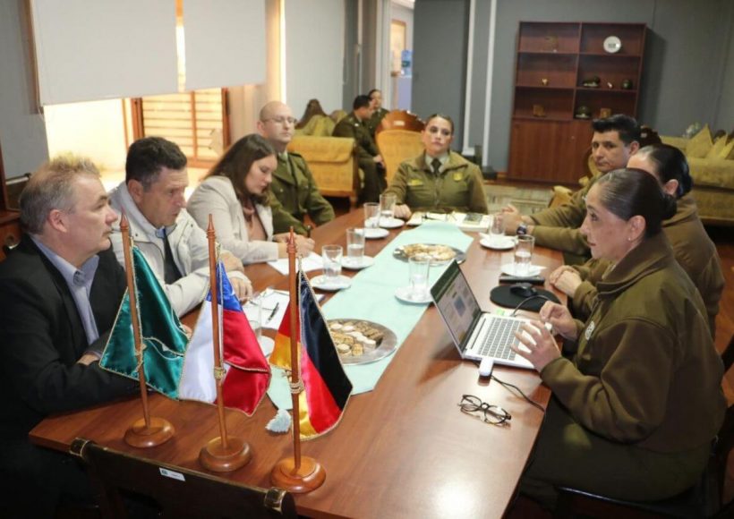 Briefing at Carabineros office; desk flags and laptop in foreground as officers and GS-Foundation delegates confer.