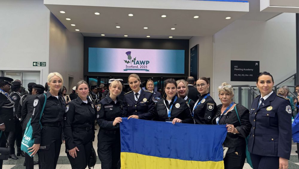 Kateryna Pavlichenko together with Ukrainian police officers holding the national flag in the conference lobby at IAWP Scotland 2025.