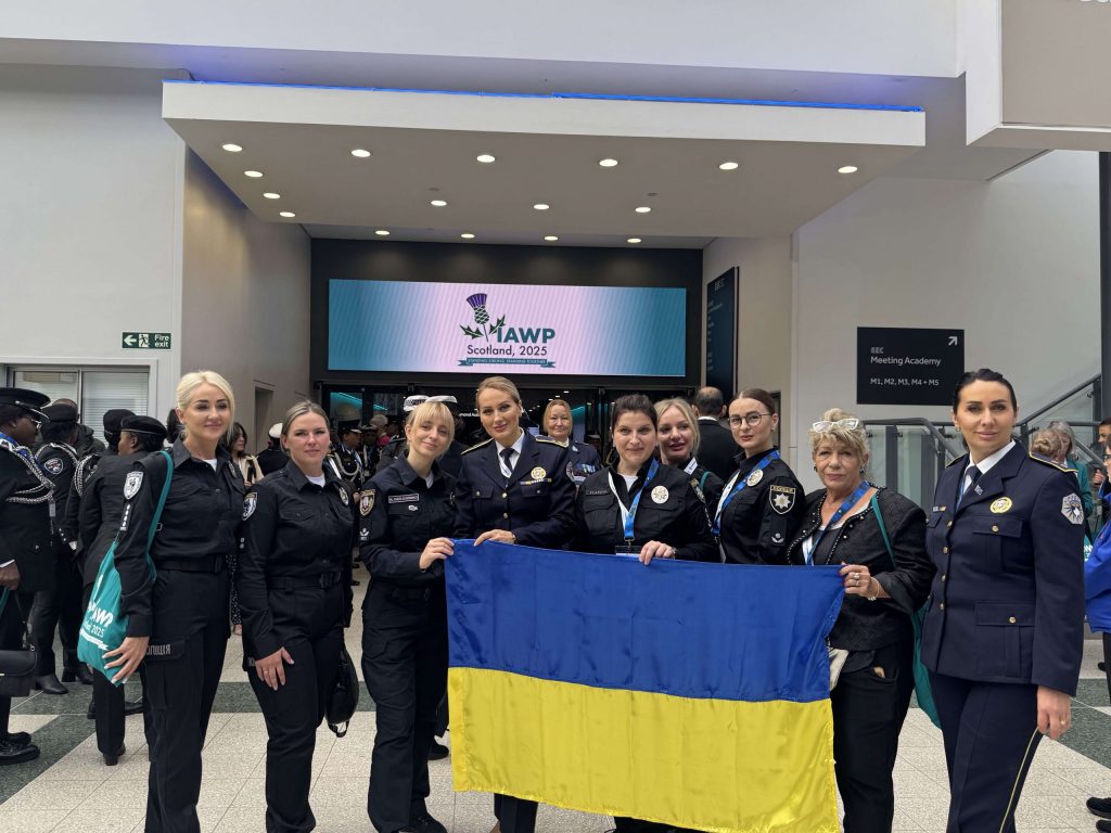 Kateryna Pavlichenko together with Ukrainian police officers holding the national flag in the conference lobby at IAWP Scotland 2025.