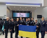 Kateryna Pavlichenko together with Ukrainian police officers holding the national flag in the conference lobby at IAWP Scotland 2025.