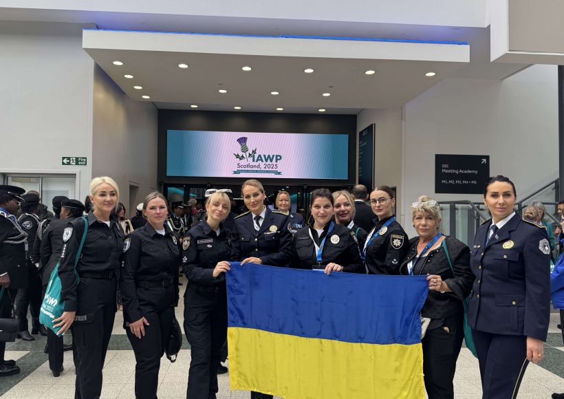 Kateryna Pavlichenko together with Ukrainian police officers holding the national flag in the conference lobby at IAWP Scotland 2025.